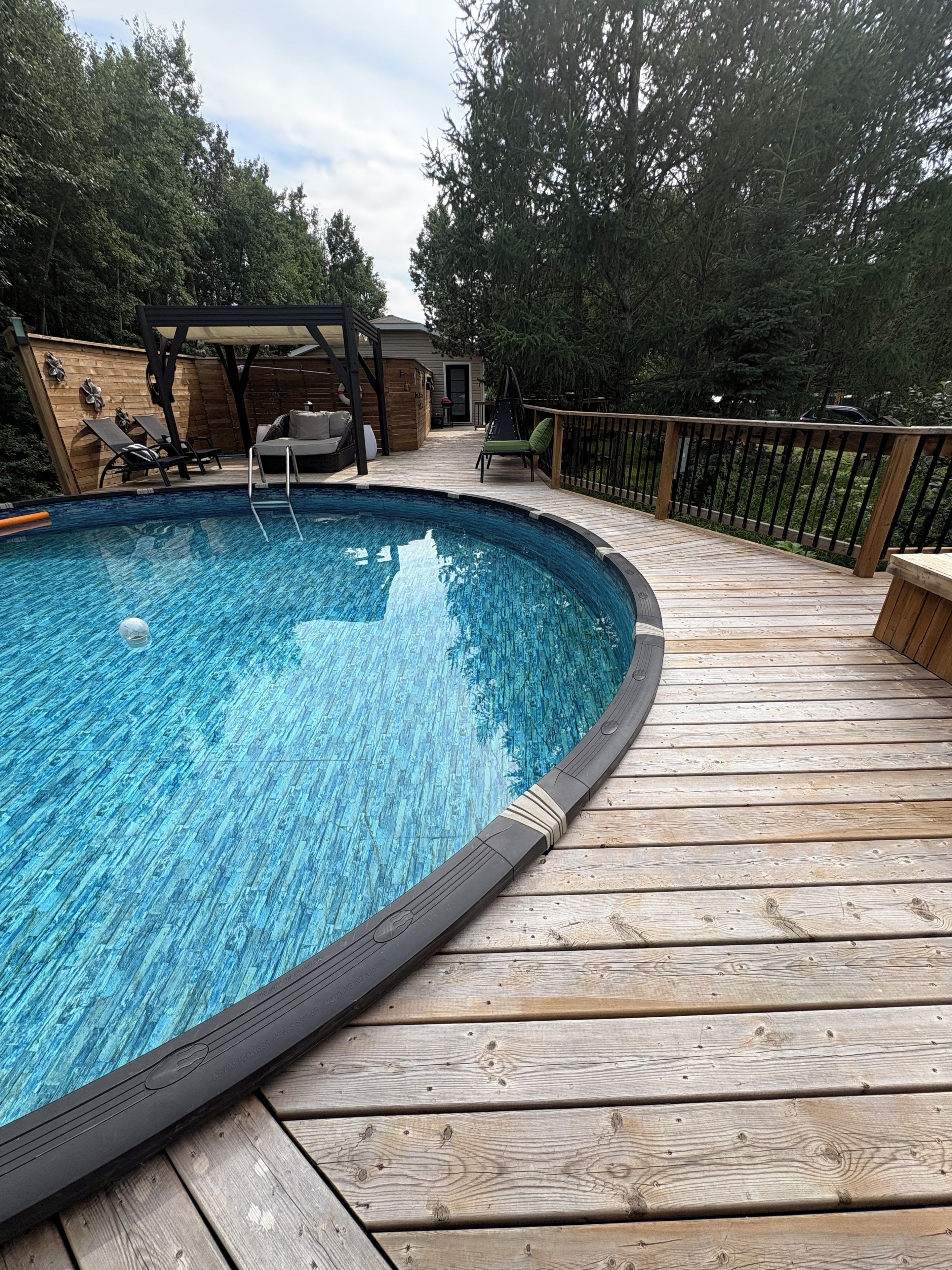 A wooden deck surrounding a swimming pool with lounge chairs and a covered seating area.