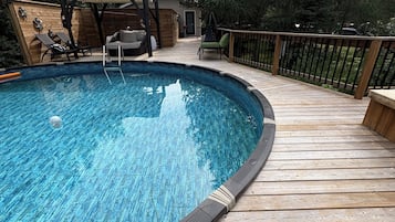 A wooden deck surrounding a swimming pool with lounge chairs and a covered seating area.
