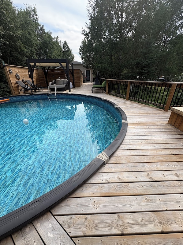A wooden deck surrounding a swimming pool with lounge chairs and a covered seating area.