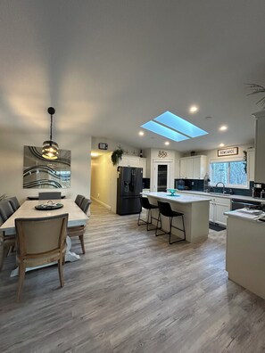 A modern kitchen with a central island, a dining area with a table and chairs, and a ceiling skylight.