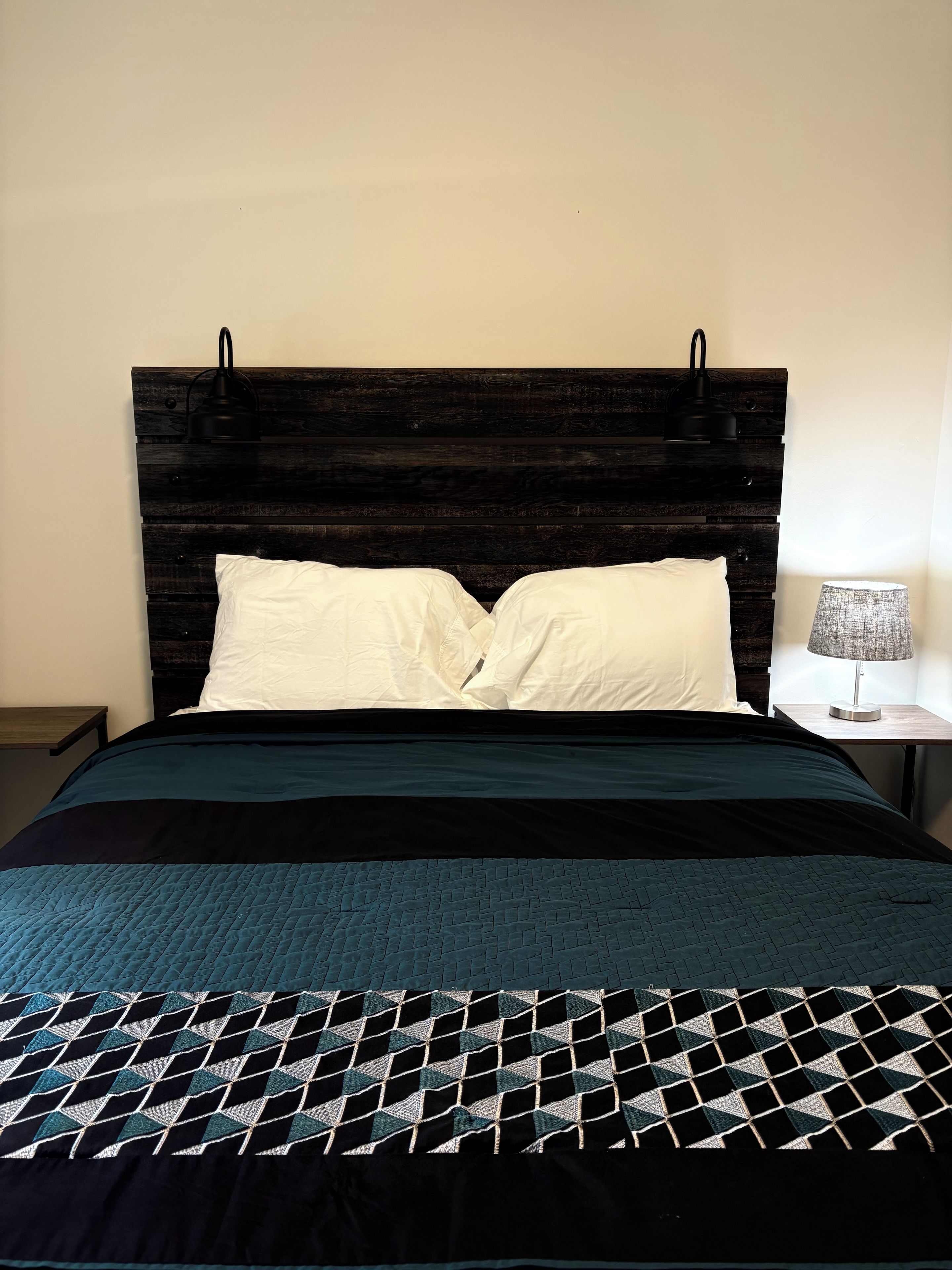 A bed with a dark wooden headboard, white pillows, and a patterned bedspread.