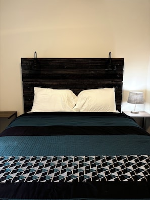 A bed with a dark wooden headboard, white pillows, and a patterned bedspread.