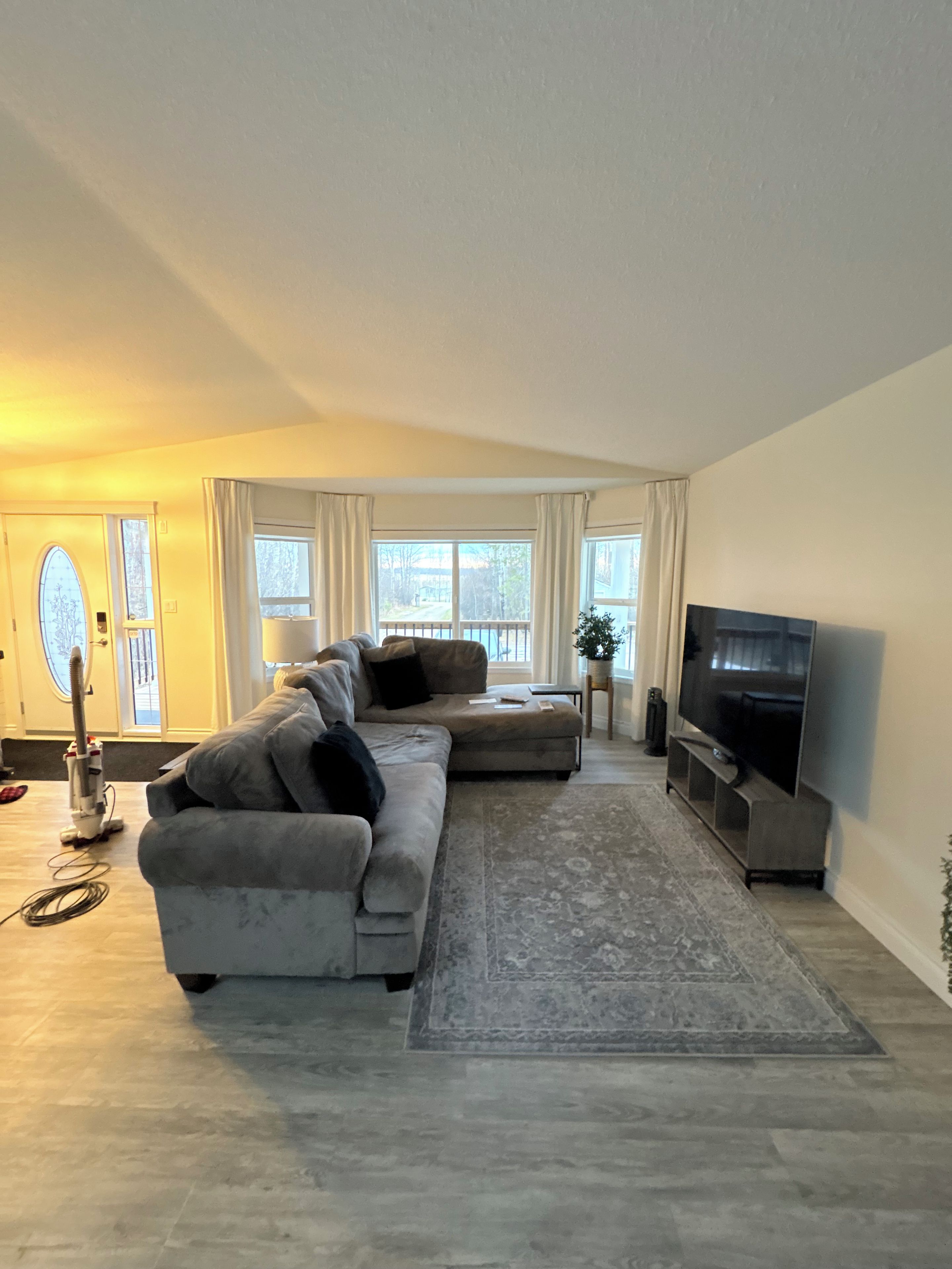 A modern living room with a sectional sofa, a flat-screen TV, and a large window providing a view of the outdoors.