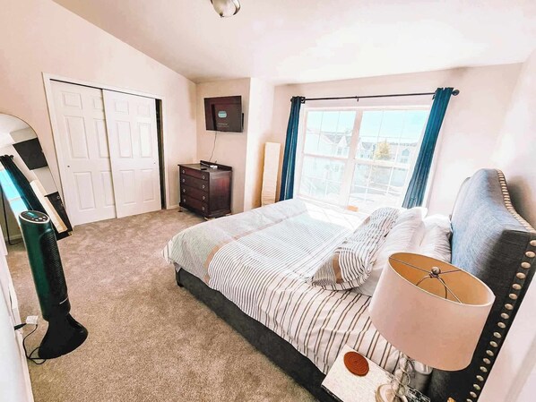 A bedroom with a bed, a dresser, a TV, a window with curtains, and a lamp.