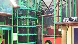 Ein Spielbereich mit roten und grünen Spielgeräten, darunter eine Kletterwand und eine Rutsche.