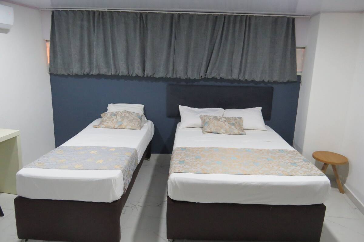 Une chambre d’hôtel avec deux lits simples, une petite table ronde et un rideau gris.