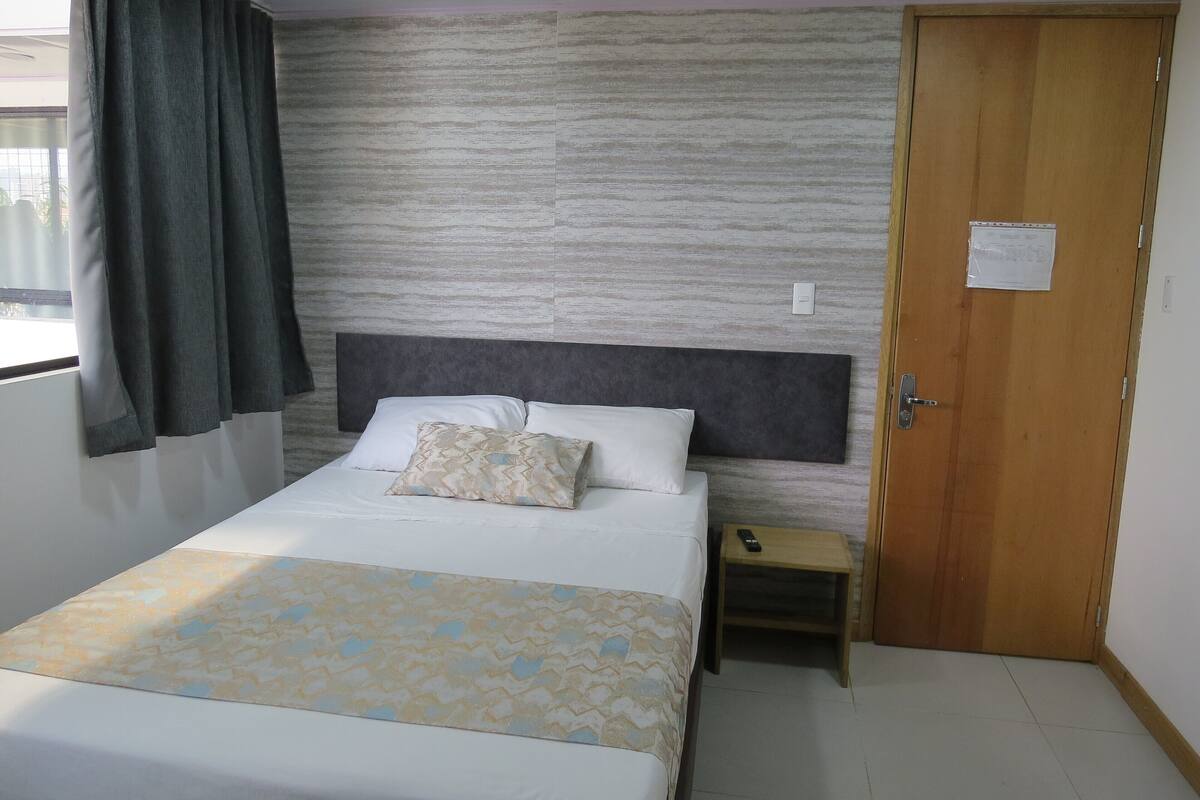 Une chambre d’hôtel avec un lit, une table de chevet, une porte en bois et une fenêtre avec des rideaux.