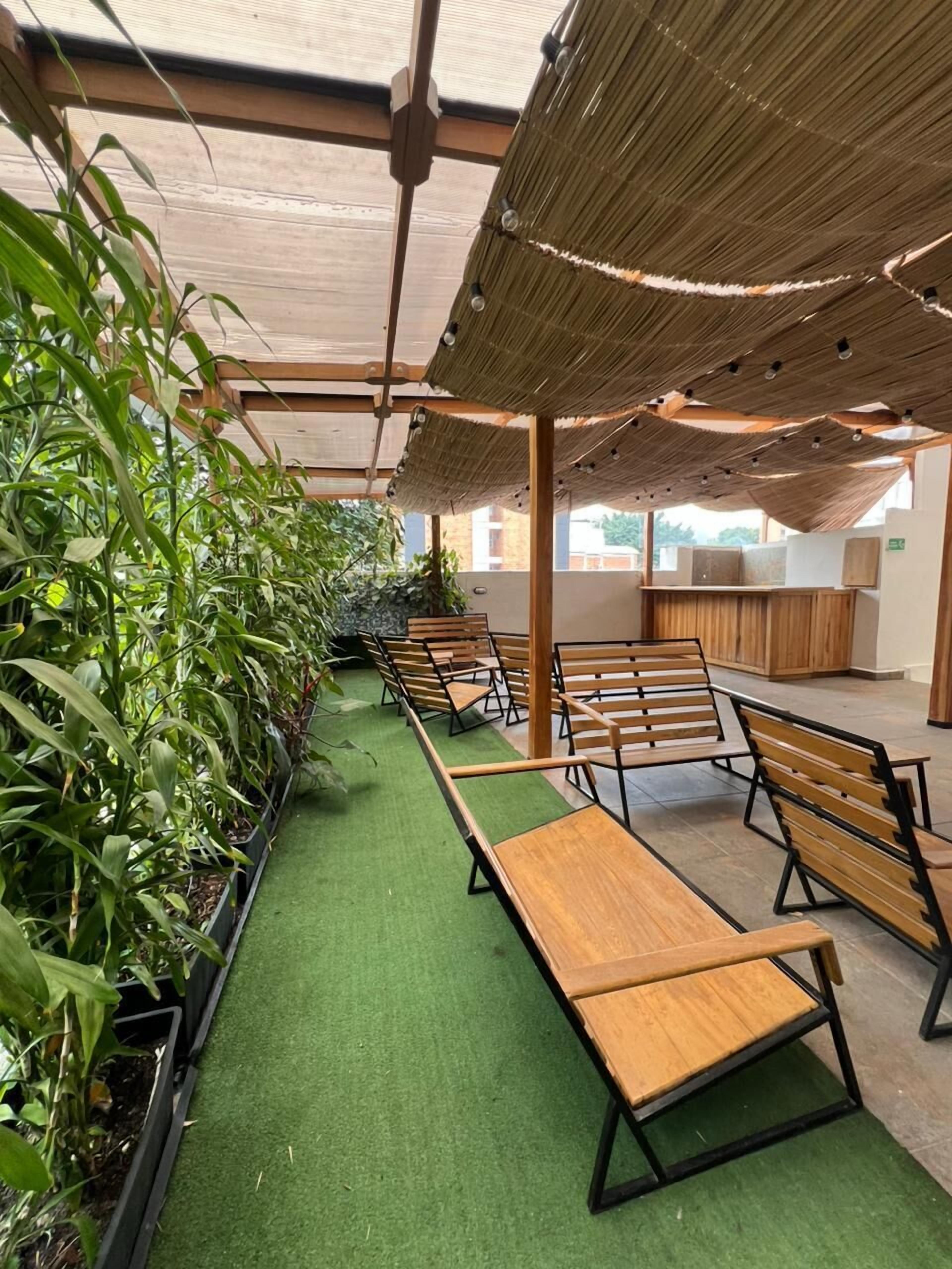 A covered outdoor seating area with wooden benches and green artificial turf.