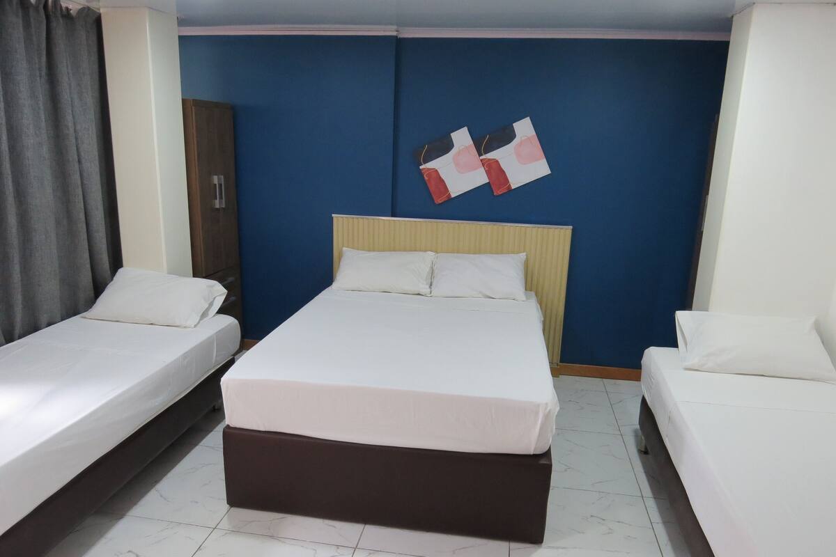 Une chambre d’hôtel avec un grand lit, deux petits lits, une armoire et un mur décoré de motifs rouges et blancs.