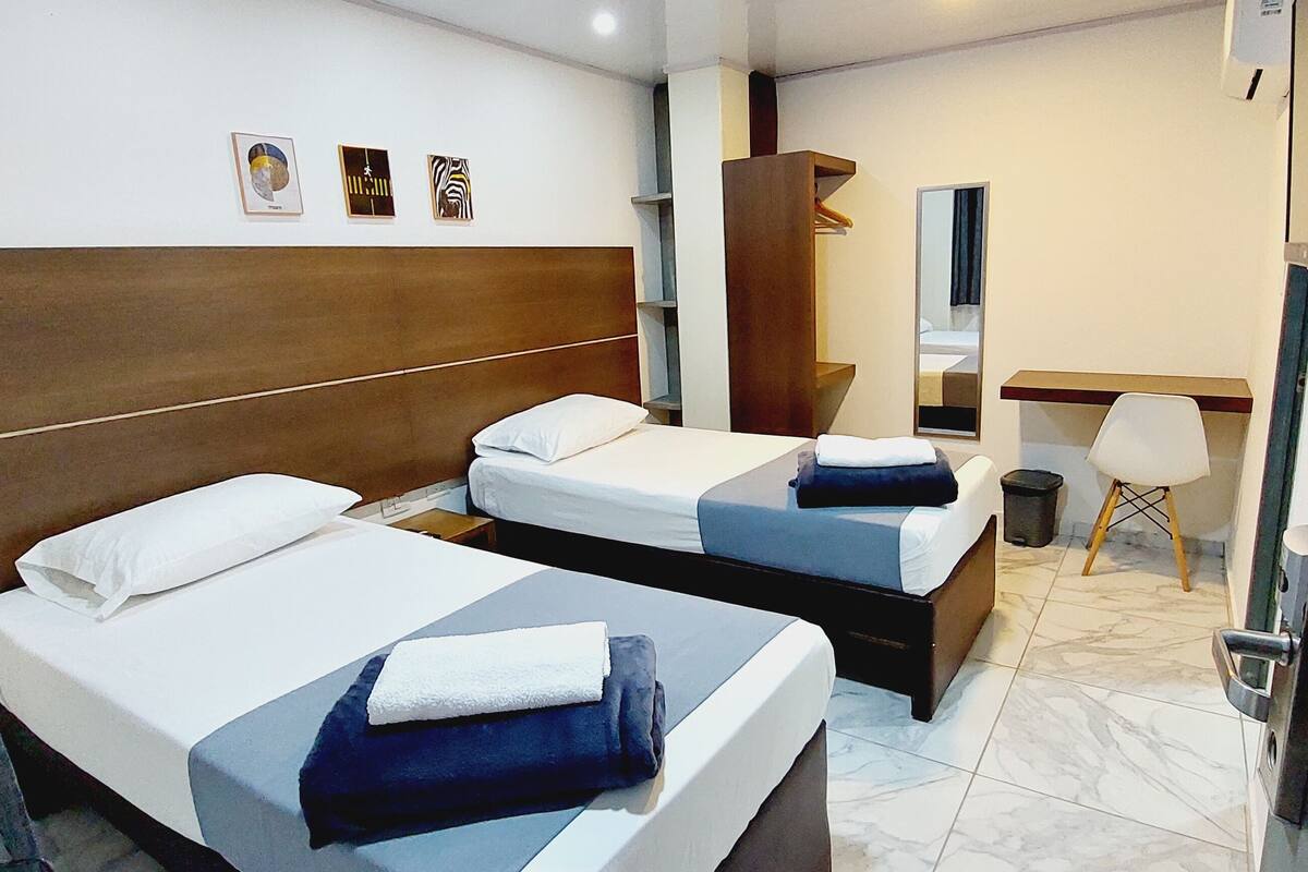 Une chambre d’hôtel avec deux lits, un bureau, une chaise, un miroir et une armoire.