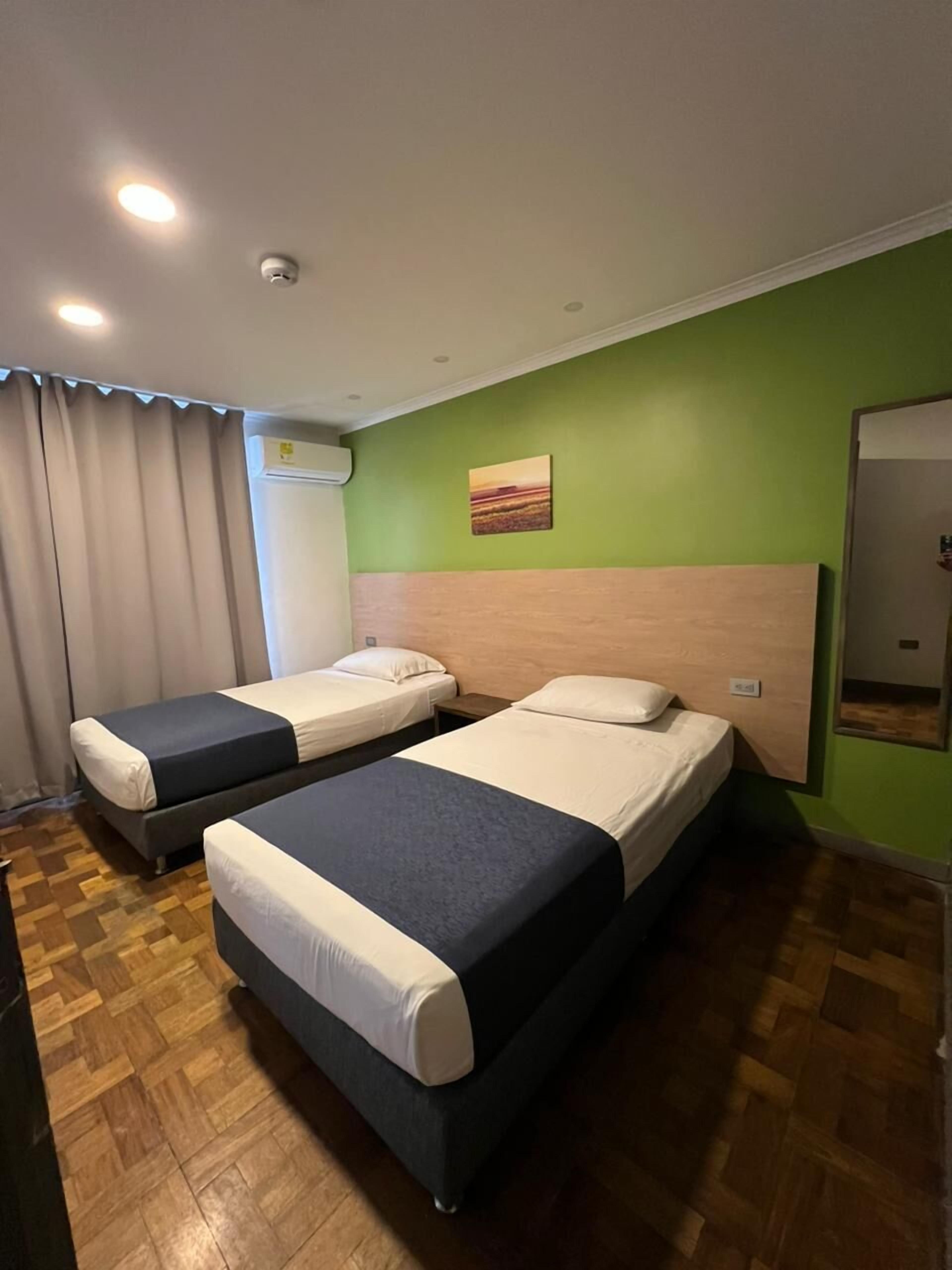 A hotel room with two beds, a green wall, a painting, and a mirror.