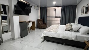 Un dormitorio moderno con cama, escritorio, silla y televisor en la pared.