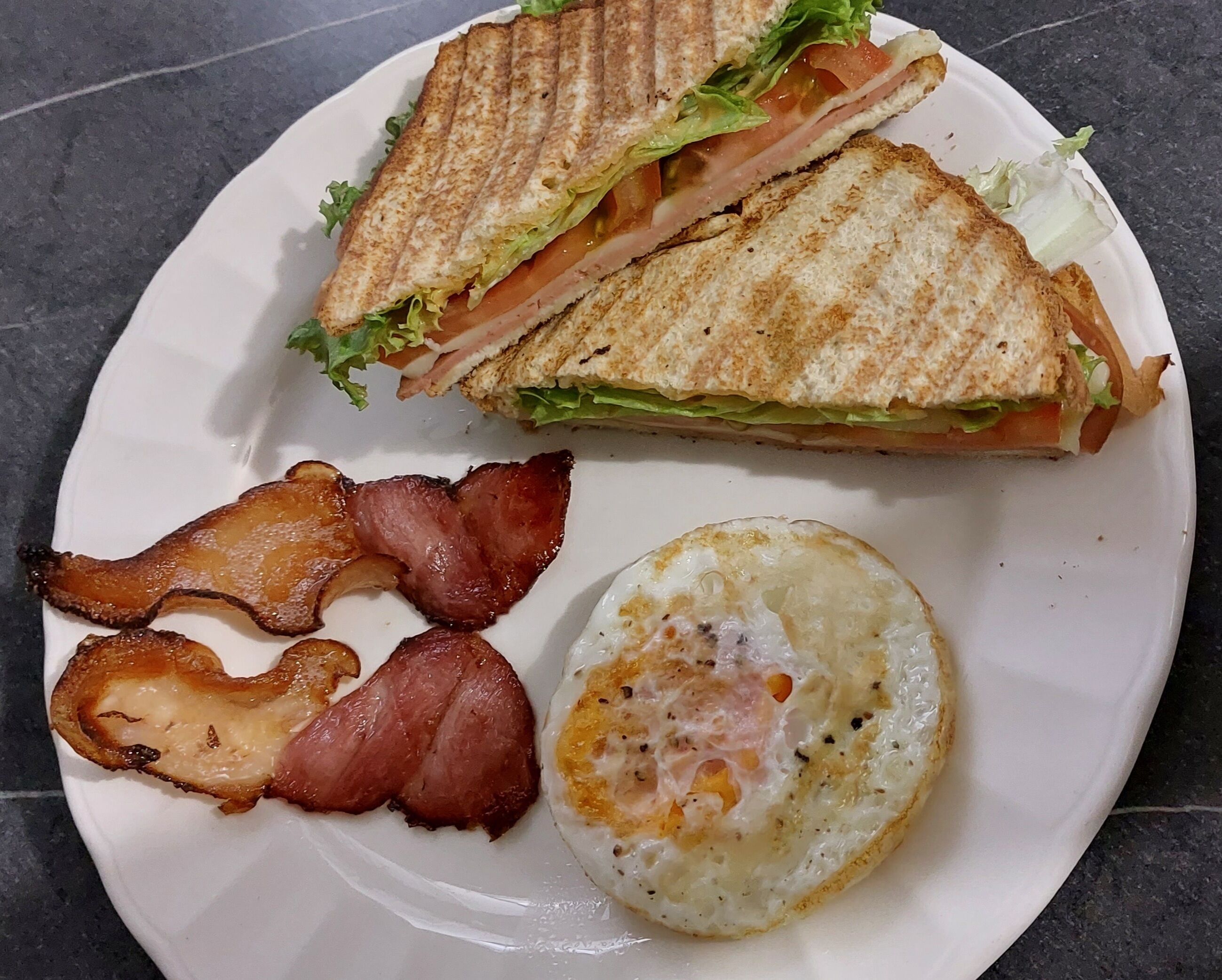 A plate with a grilled sandwich, bacon, and a fried egg.