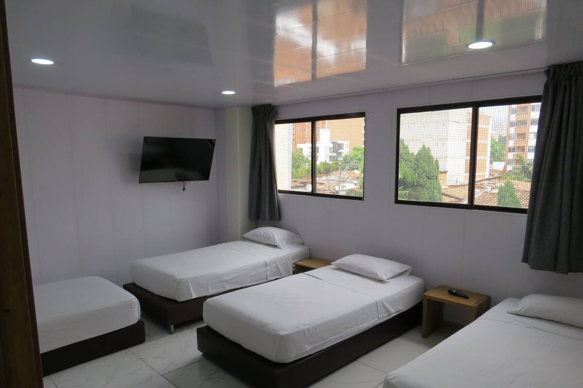 Une chambre d’hôtel avec trois lits simples, un téléviseur fixé au mur et de grandes fenêtres donnant sur la ville.