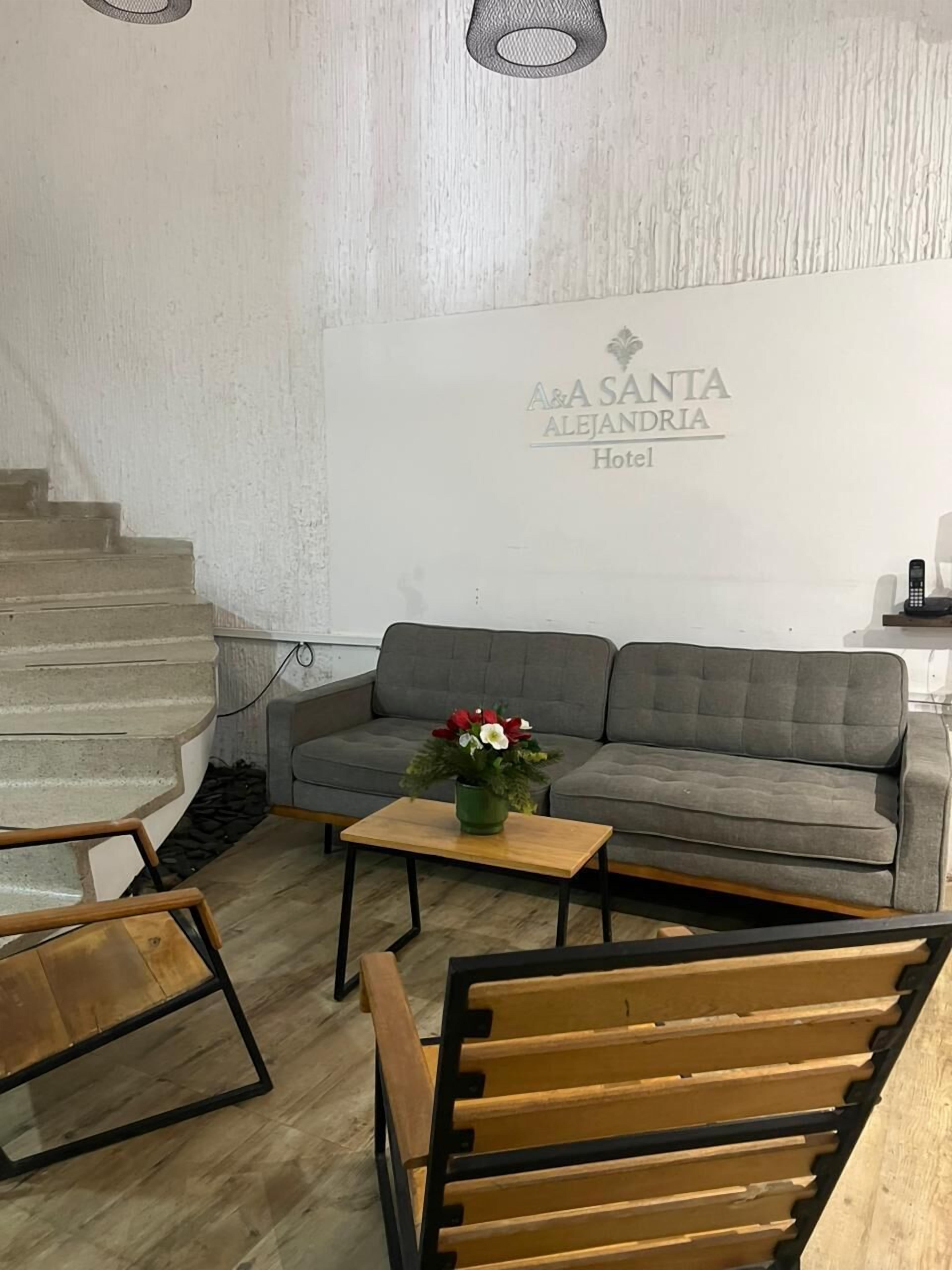A hotel room with a grey sofa, a wooden coffee table with a flower vase, a wooden bench, and a staircase.