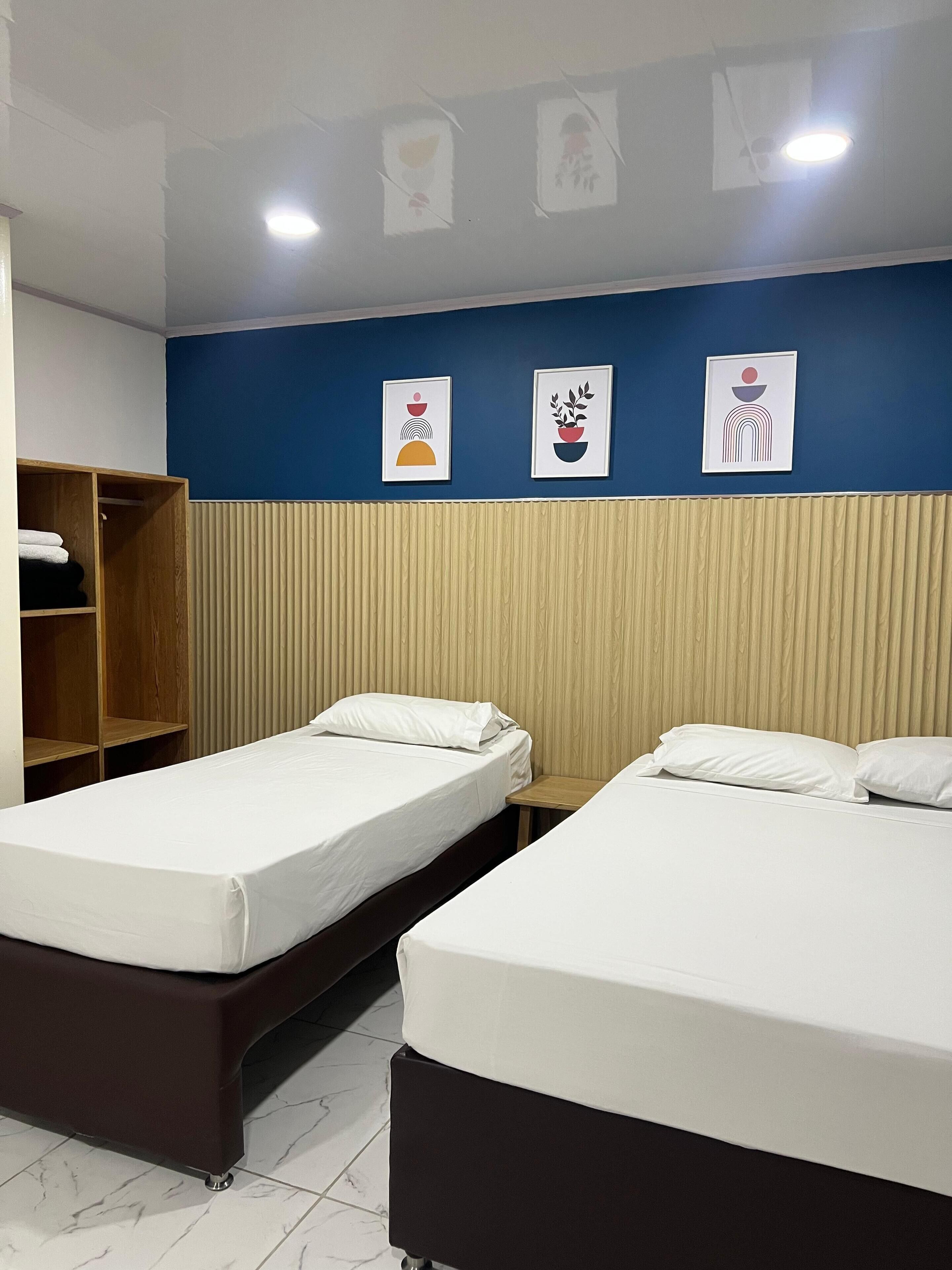 A hotel room with two beds, a wooden wardrobe, and a wall with three framed artworks.