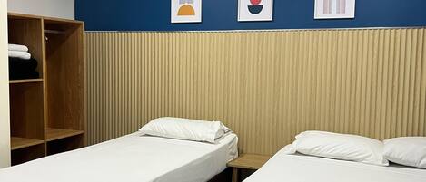 A hotel room with two beds, a wooden wardrobe, and a wall with three framed artworks.