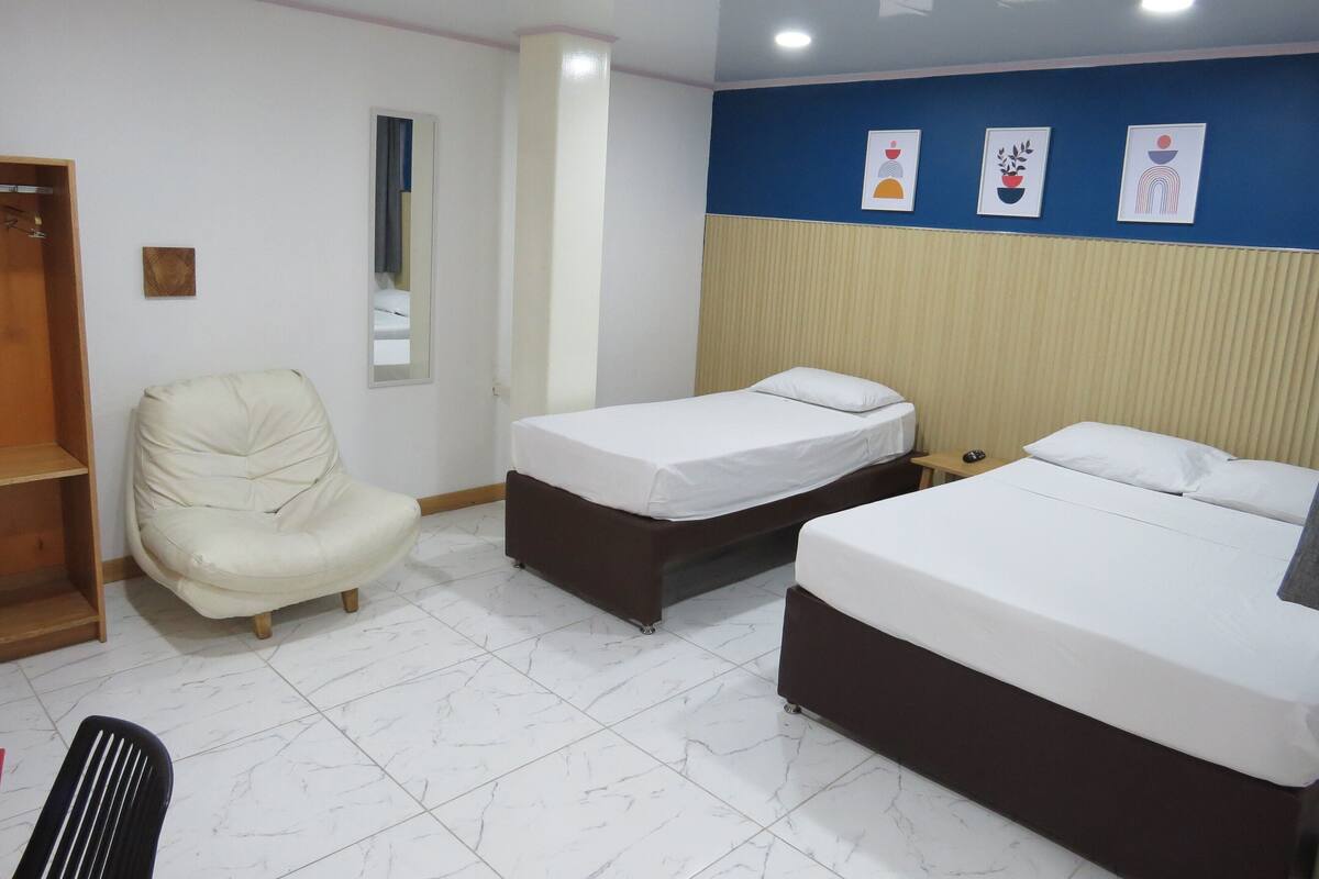 Une chambre d’hôtel avec deux lits simples, une chaise, une armoire et un miroir.