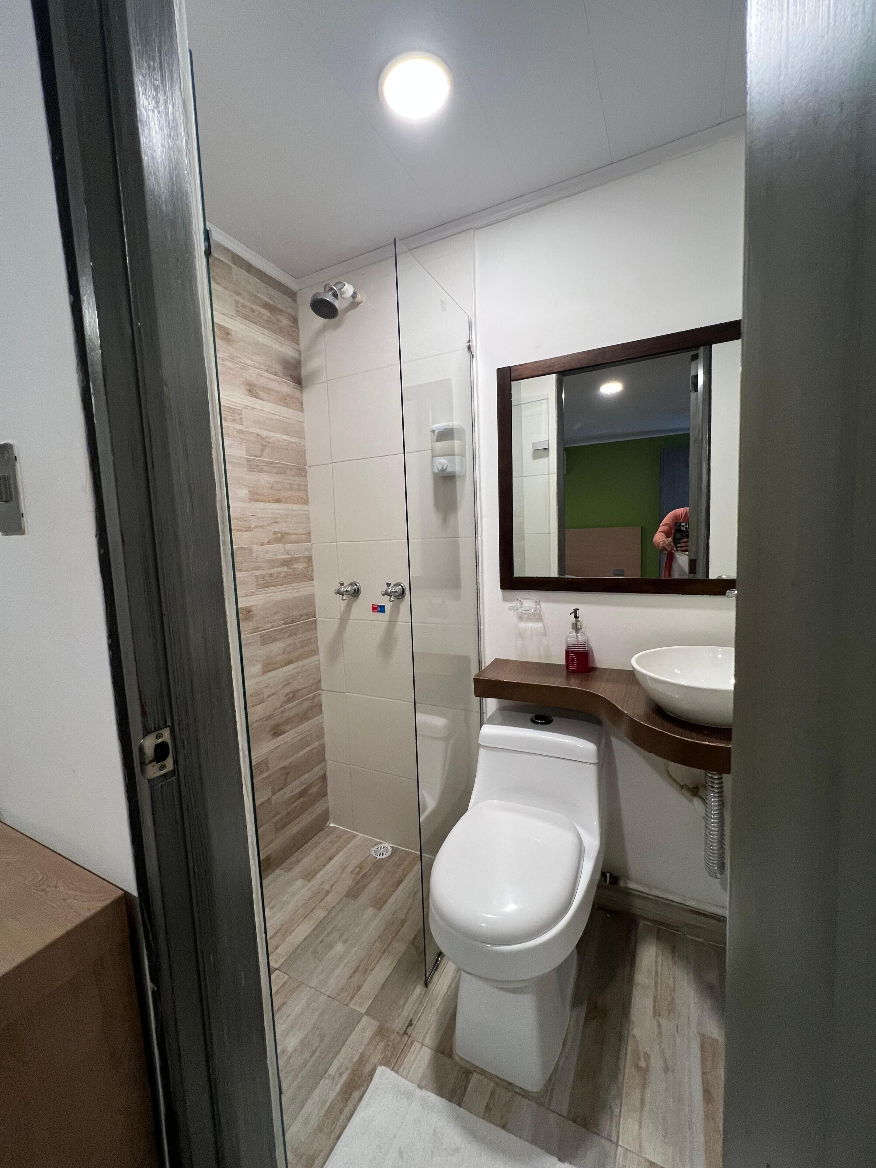 A modern bathroom with a glass shower enclosure, a white toilet, and a wooden vanity with a sink.