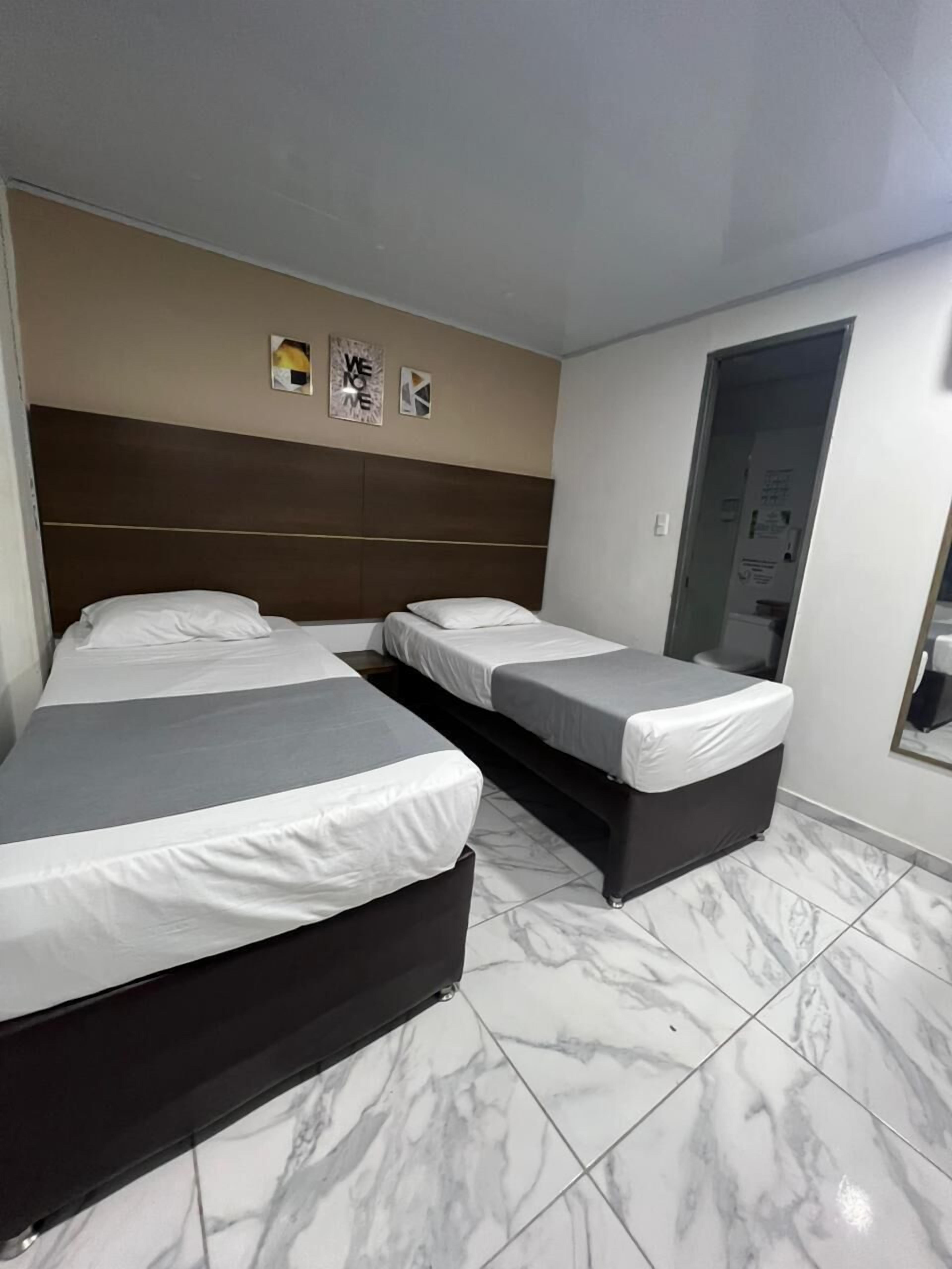 A hotel room with two beds, a marble-tiled floor, and a brown headboard.