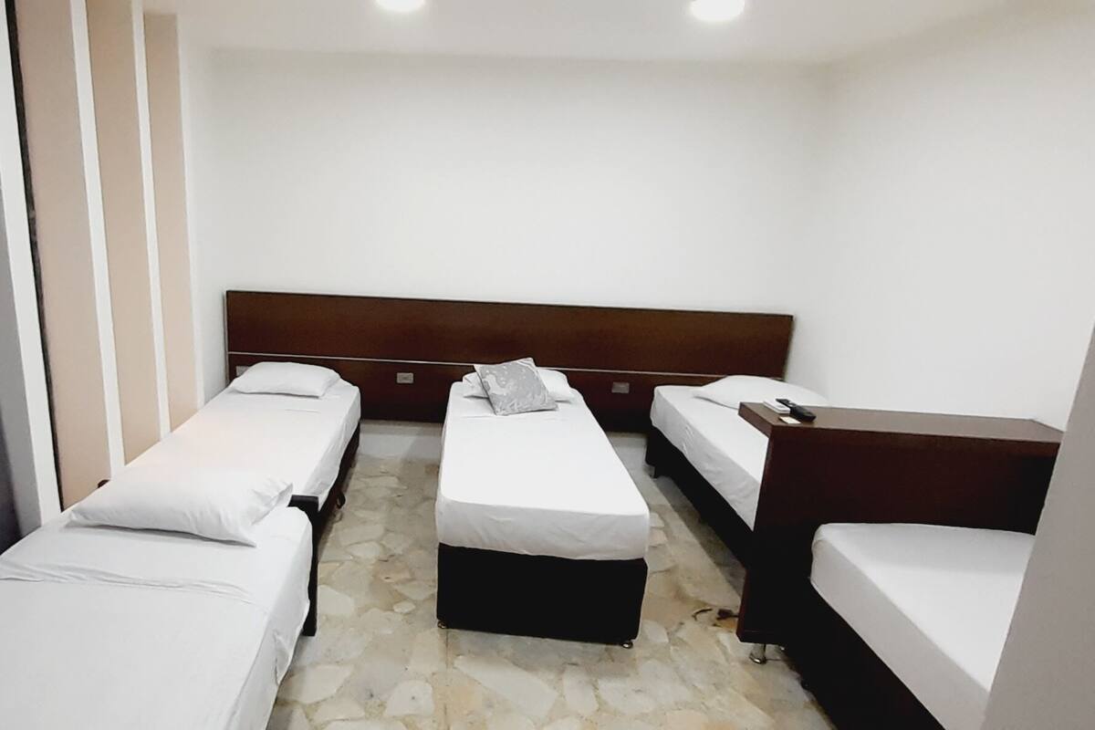 Une chambre d’hôtel avec trois lits simples, une tête de lit en bois et un sol imitant la pierre.