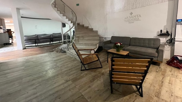 Un amplio vestíbulo de hotel con suelo de madera, una escalera, un sofá gris y un banco de madera.