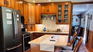 Une cuisine dotée de meubles en bois, d’un réfrigérateur en acier inoxydable, d’une cuisinière et d’un coin repas avec des chaises en bois et un tapis.