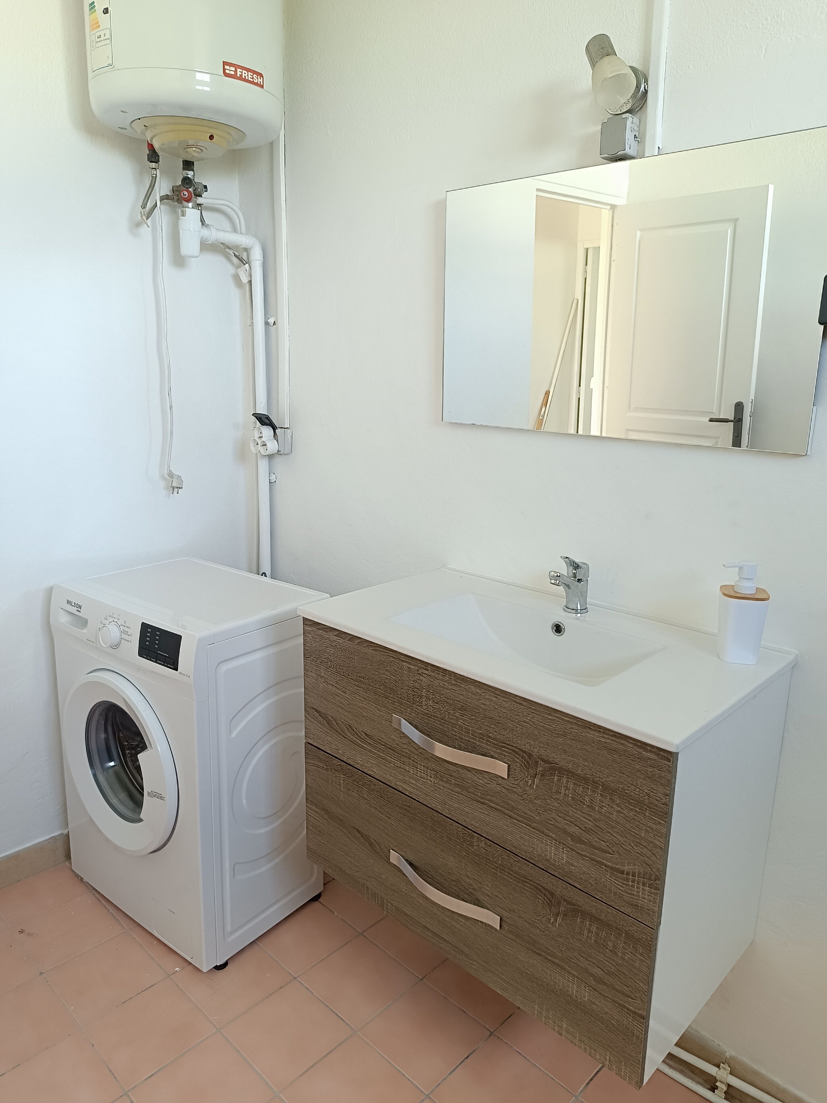 Een kleine badkamer met een wasmachine, wastafel en spiegel.