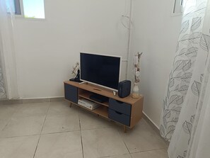A living room with a wooden TV stand, a flat-screen TV, a soundbar, and a decorative Buddha statue.