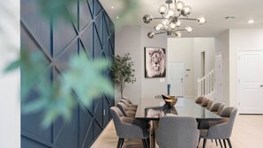 A modern dining area with a glass table, grey chairs, a decorative chandelier, and a blue accent wall. - 8BR house sleeps 16 with private pool (Davenport)