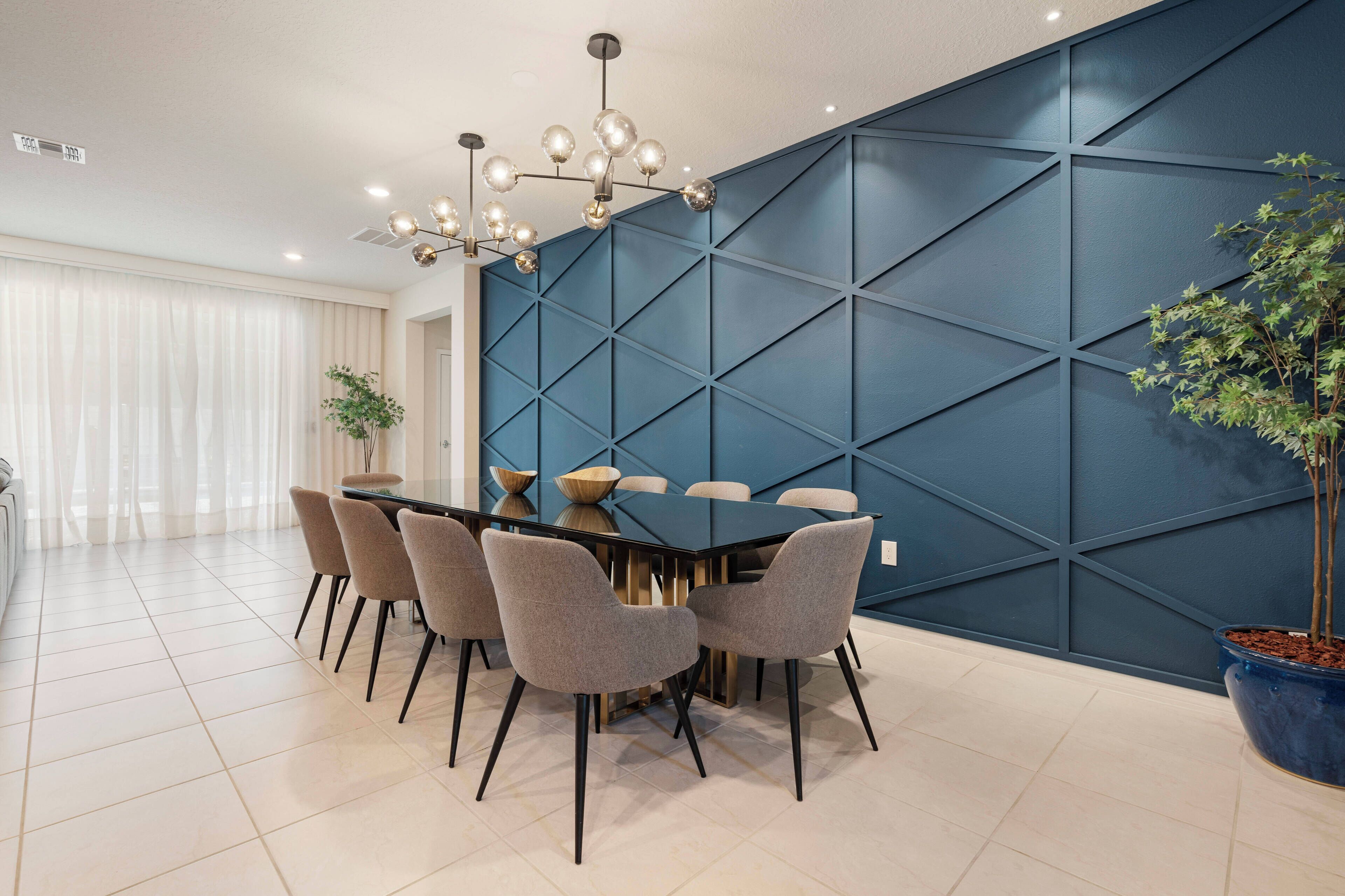 A modern dining area with a round table, six chairs, a blue accent wall, and a chandelier.