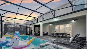 Una piscina interior con flotadores de unicornio inflables, una bañera de hidromasaje y un patio con mobiliario exterior.