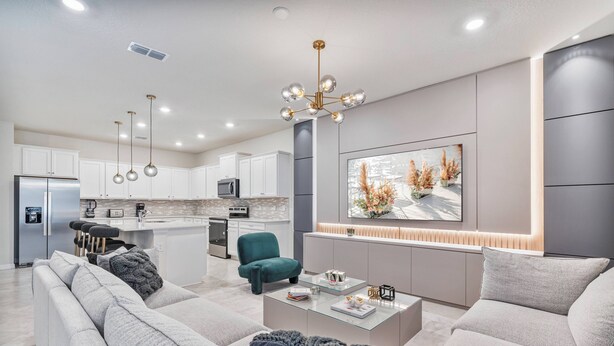 Una sala moderna con sofá, mesa de centro y un sillón color turquesa. Se ve, en el fondo, una cocina con armarios blancos y un comedor.