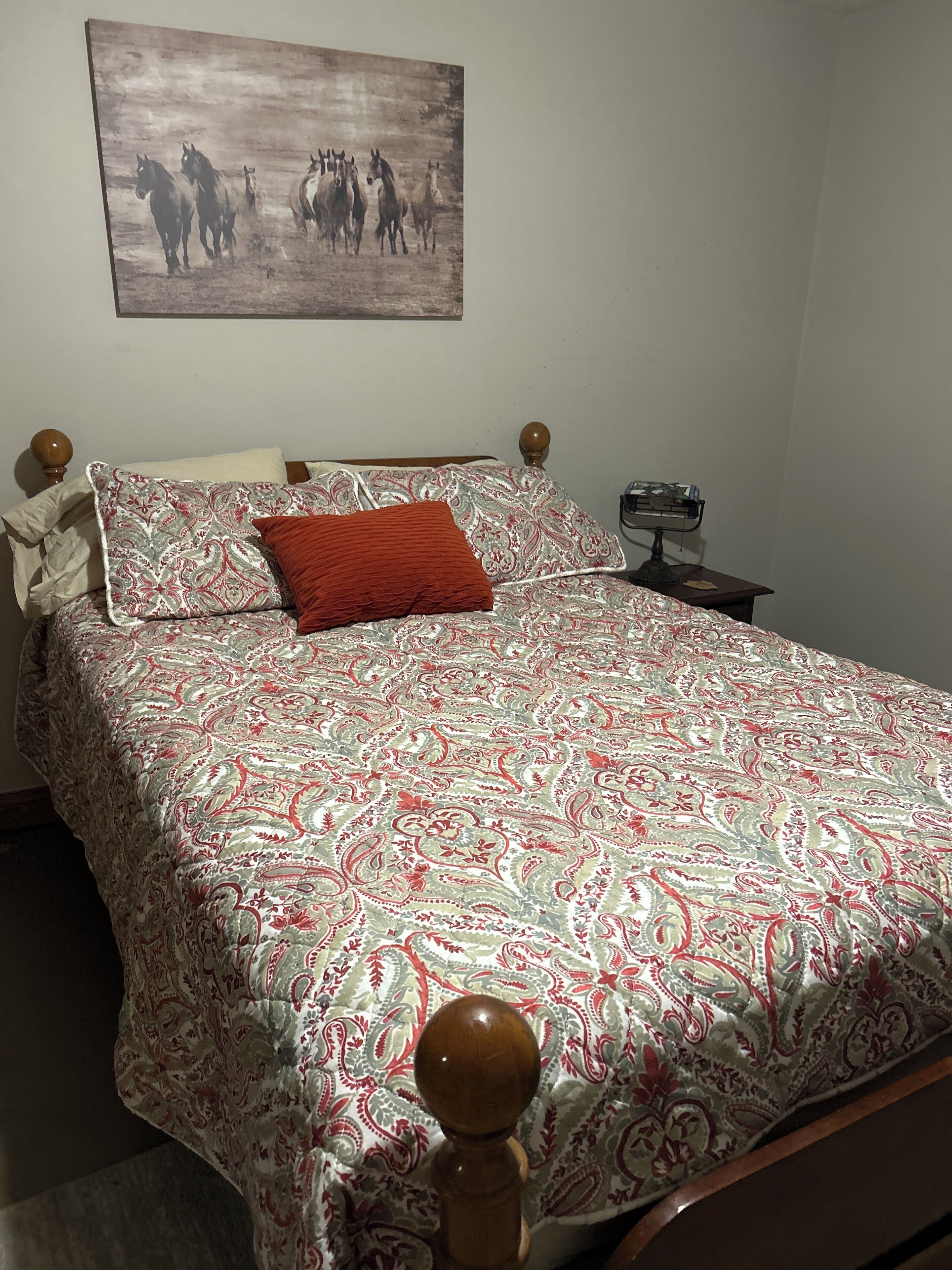 Een netjes opgemaakt bed met een beddengoed met patroon, een rood kussen en een houten hoofdbord.