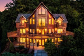 Une grande cabane en bois, dotée de nombreux balcons et de grandes fenêtres, entourée d’une forêt dense.