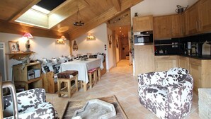 A cozy, rustic interior with a dining area, a living room with a patterned sofa, and a kitchen with wooden cabinets.