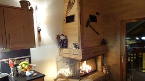 A cozy kitchen with a stone fireplace, wooden cabinets, and a fruit bowl on the counter.