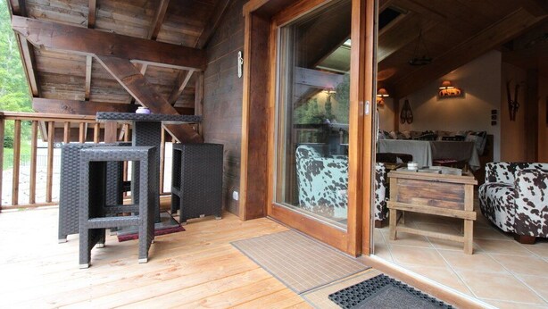 A wooden deck with outdoor furniture, a sliding glass door leading to an interior with a sofa and a table.