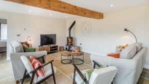 A modern living room with a high ceiling, a fireplace, a television, and comfortable seating. - The Granary - UK46002 (Cranswick, near Driffield)