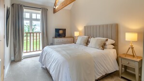 A bedroom with a large bed, two bedside lamps, a TV, and a window with curtains. - The Granary - UK46002 (Cranswick, near Driffield)