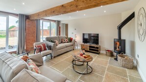 A spacious living room with a fireplace, a television, and a dining area with a table set for a meal. - The Granary - UK46002 (Cranswick, near Driffield)