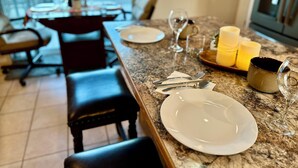 A dining area with a marble countertop, a set table with plates, cutlery, and candles, and a view of the outside through large windows. - Tranquil Foothills Retreat  (Yuma)