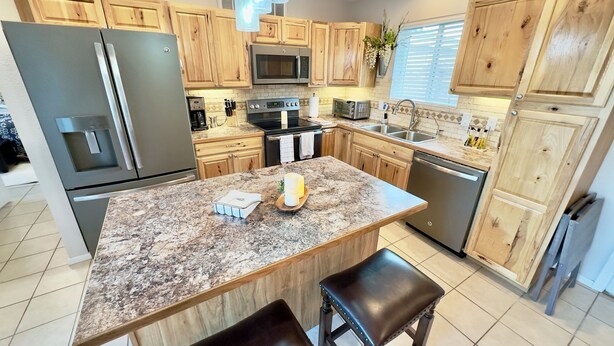 A kitchen with wooden cabinets, stainless steel appliances, a granite countertop, and a central island with stools. - Tranquil Foothills Retreat  (Yuma)