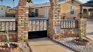 A brick archway leading to a gated entrance with a 'Welcome' sign, a patio area with a table and chairs, and a cactus plant in the foreground. - Tranquil Foothills Retreat  (Yuma)