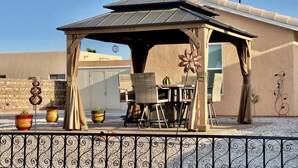 A covered patio area with outdoor furniture, a decorative wind spinner, and a brick wall. - Tranquil Foothills Retreat  (Yuma)