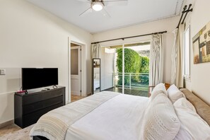 A bedroom with a bed, a TV on a dresser, a ceiling fan, and a balcony with curtains. - Ocean Front Hot tub Pool Kite Beach Condo 101 (Kite Beach)