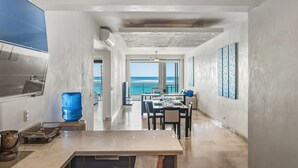 A modern kitchen with a large island, a dining area with a view of the ocean, and a spacious living area with a large window overlooking the sea. - Kite Beach • Oceanfront • Pool & Hot Tub 203 (Kite Beach)