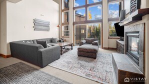 A spacious living room with a gray sectional sofa, a patterned ottoman, and a fireplace.