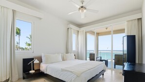 Un dormitorio amplio con una cama grande, un ventilador de techo y vistas al océano a través de amplias ventanas.
