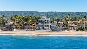 Un hotel frente a la playa con varias construcciones, palmeras y vistas al océano.